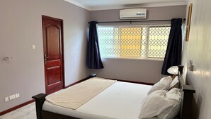 A bedroom with a bed, a window with curtains, an air conditioning unit, and a door.