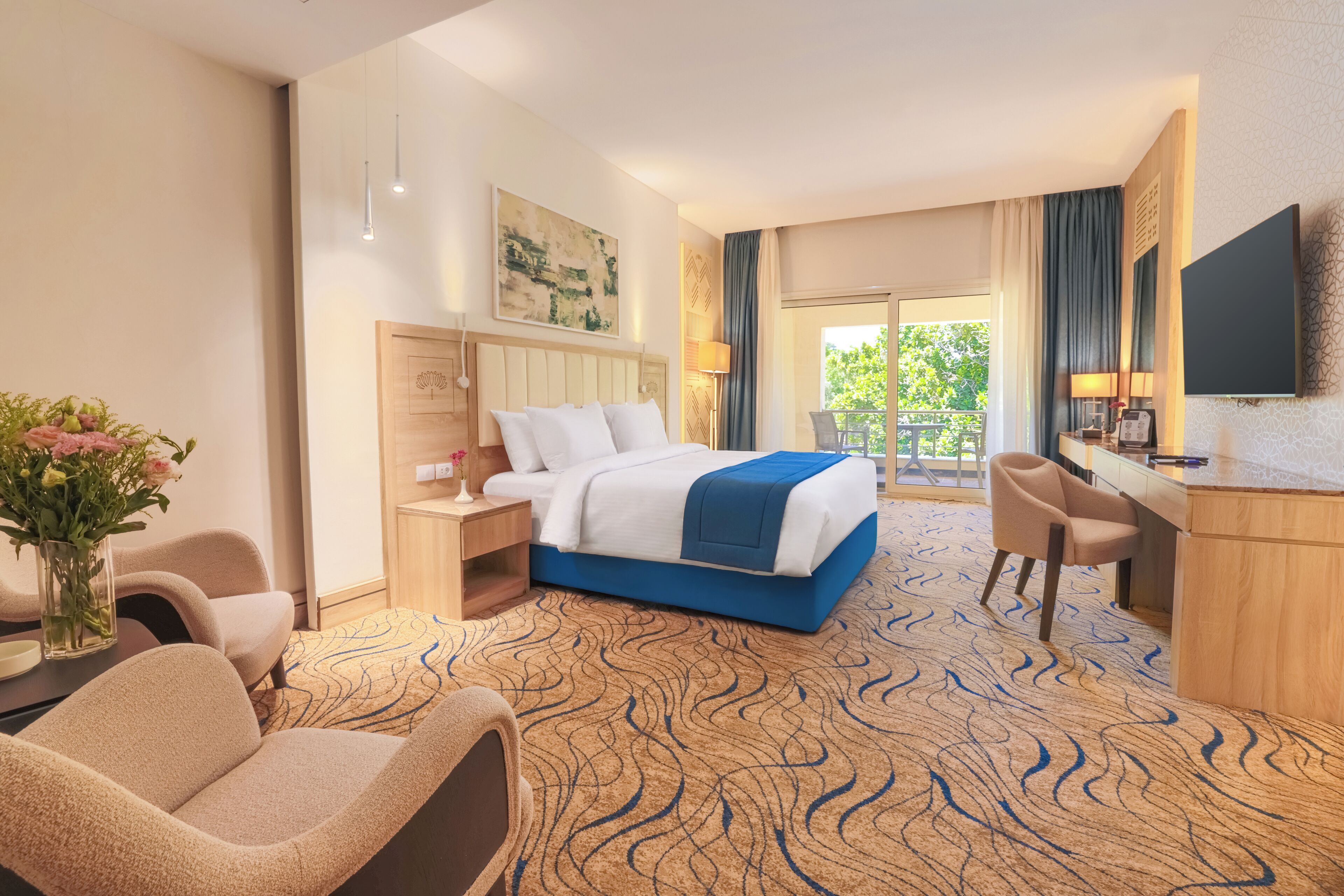 Ein Hotelzimmer mit einem großen Bett, einem Schreibtisch, einem Sessel, einem Fernseher und Blick ins Freie.