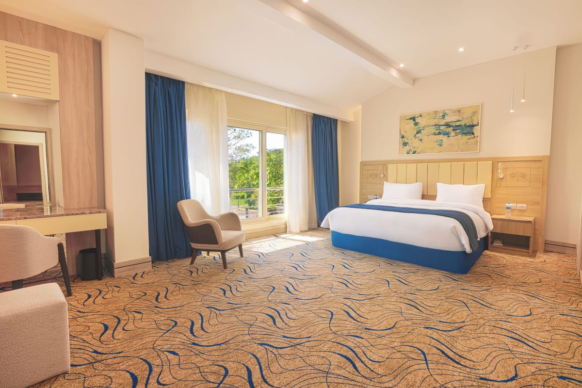A hotel room with a large bed, a desk, a chair, and a window with curtains.