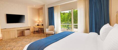 A hotel room with a large bed, a desk, a chair, a TV, and a balcony with curtains.