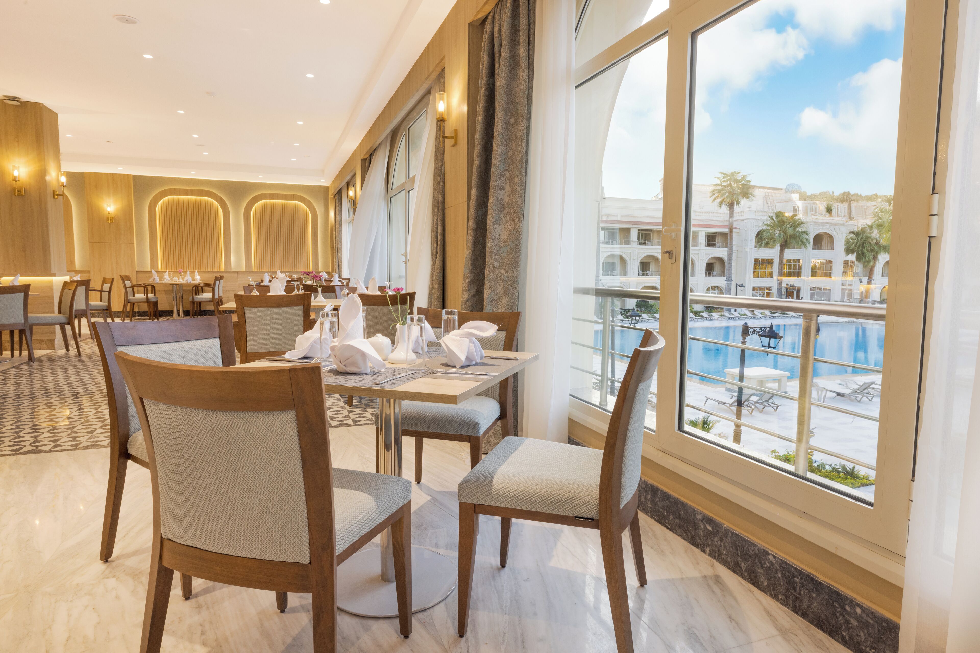 Ein Restaurant mit Blick auf einen Pool und Gebäude. Die Tische sind mit weißen Tischdecken und Servietten gedeckt.