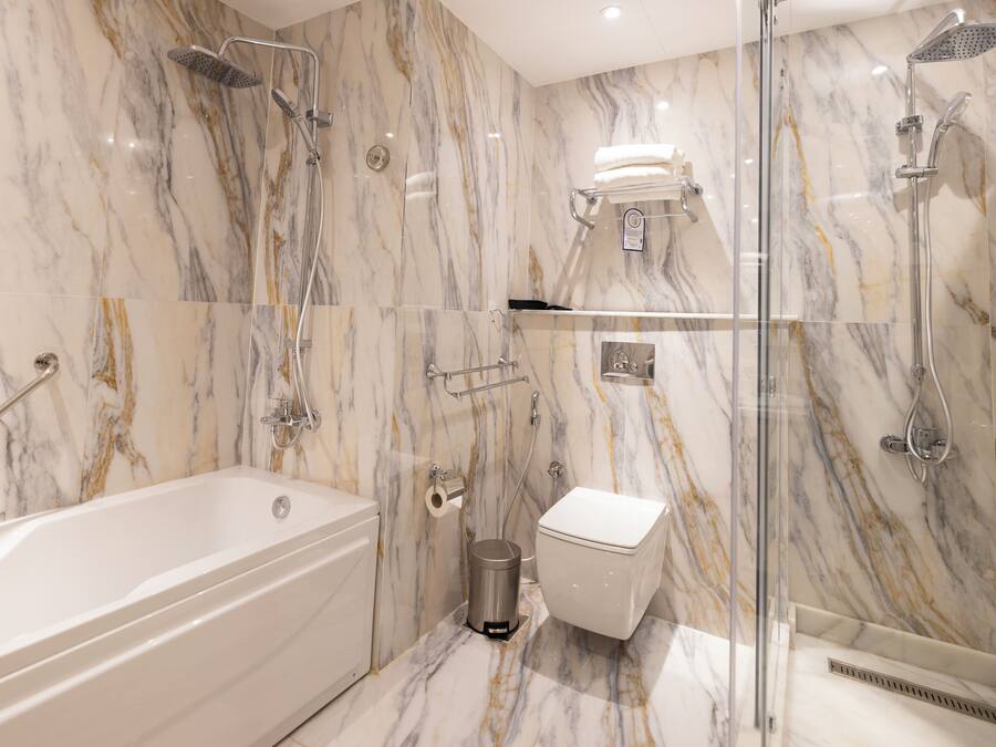 Un baño moderno con pared de mármol, una bañera, un inodoro y zona de ducha con mampara de vidrio.