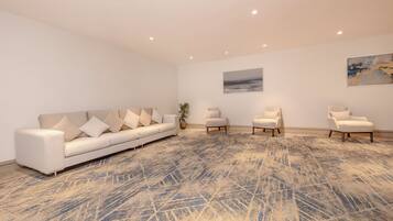 A spacious room with a large sofa, several armchairs, and a patterned carpet.