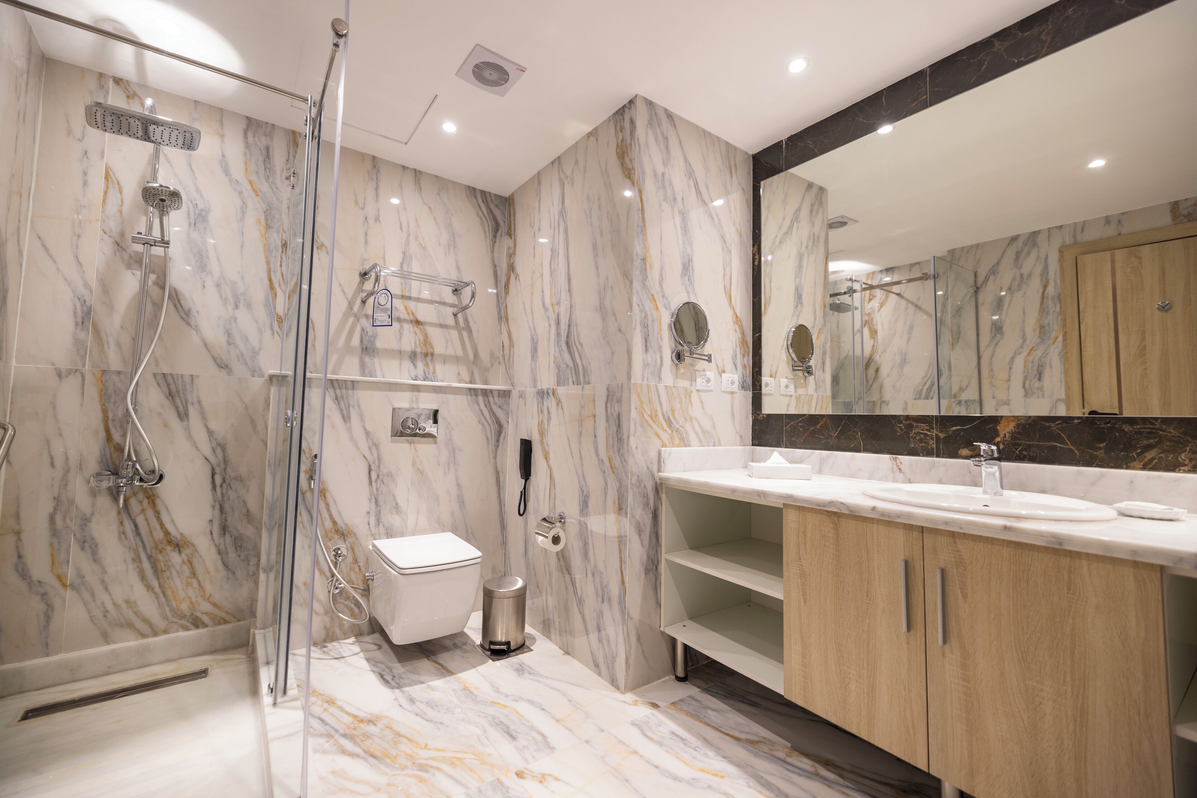Un baño moderno con ducha de vidrio, inodoro, lavamanos y tocador con espejo.
