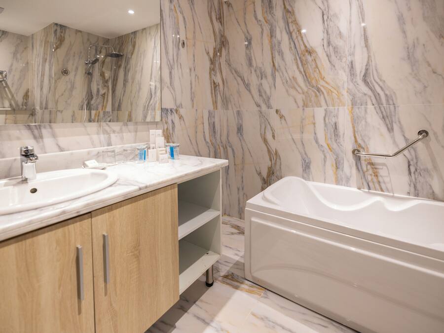 A modern bathroom with marble walls, a bathtub, and wooden cabinets.