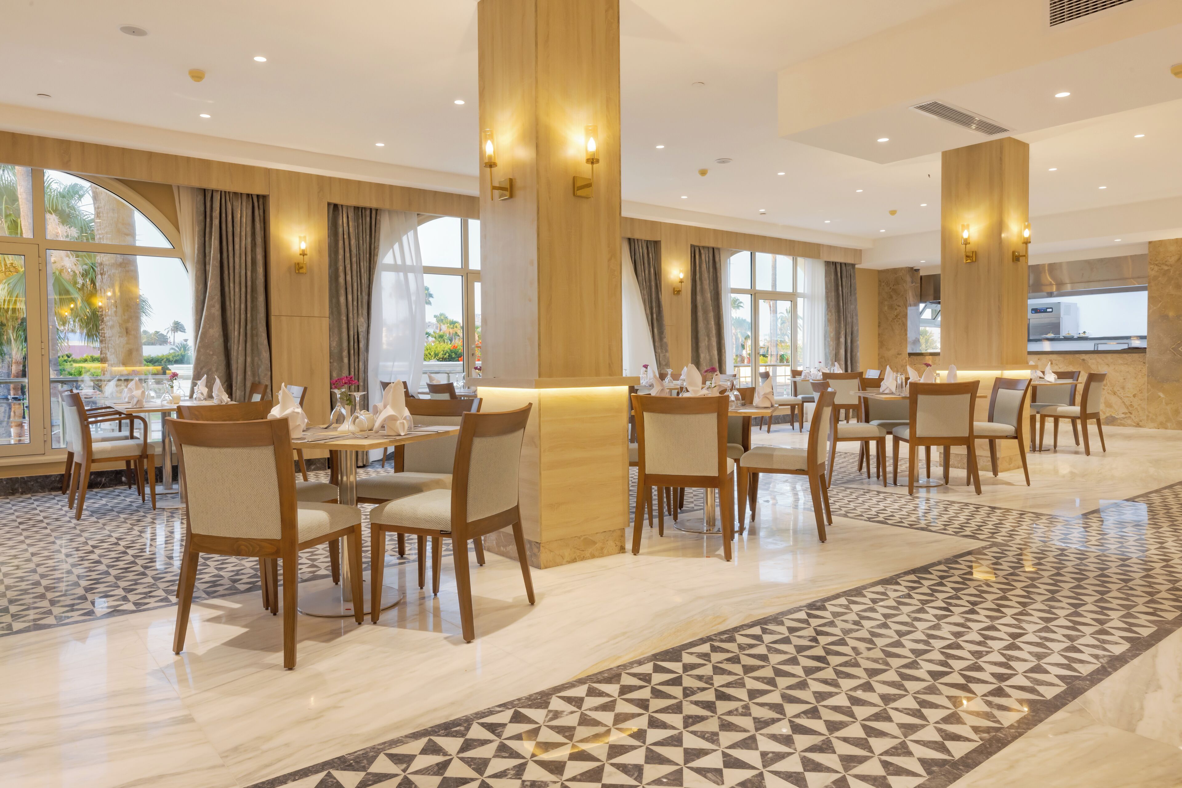 A spacious dining area with multiple tables and chairs, large windows, and a patterned floor.