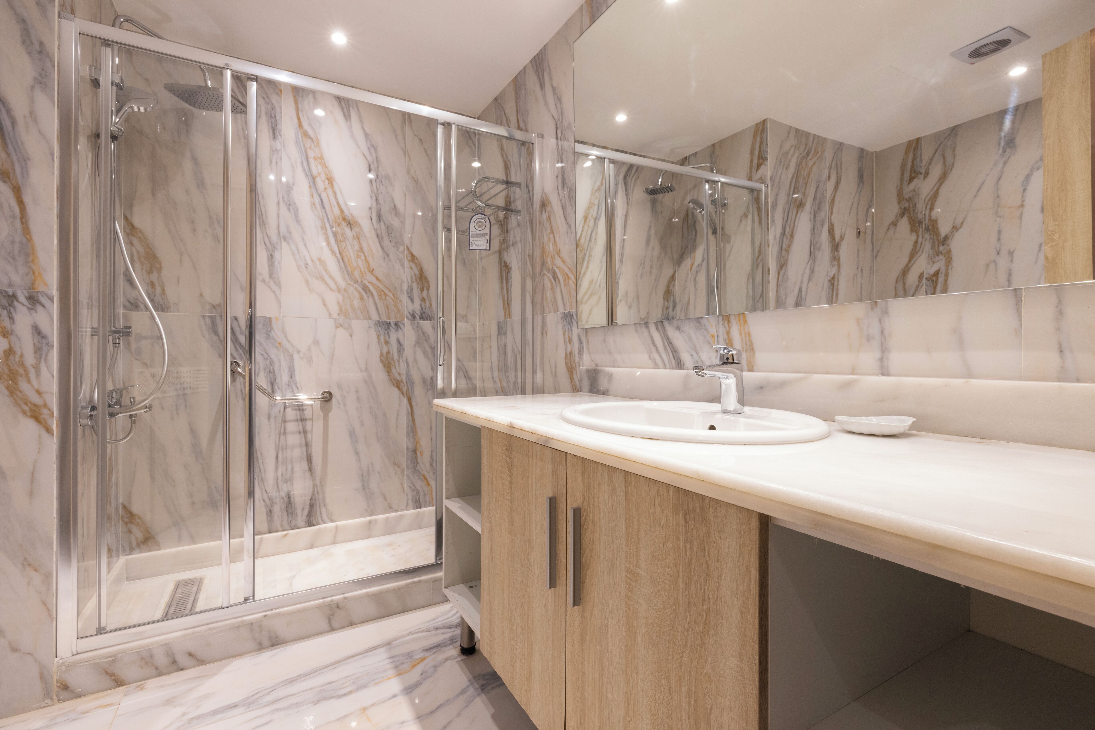 Un baño moderno con ducha envuelta en vidrio, lavamanos y paredes de mármol.