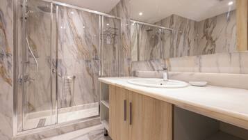 Un baño moderno con ducha envuelta en vidrio, lavamanos y paredes de mármol.