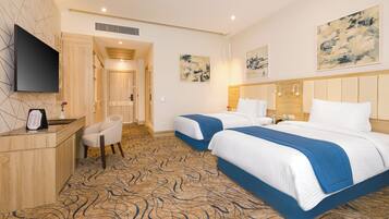 A hotel room with two beds, a desk, a chair, a flat-screen TV, and artwork on the walls.