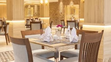 Un espace repas avec des tables et des chaises en bois, un vase rempli de fleurs et, en arrière-plan, un mur en pierre.