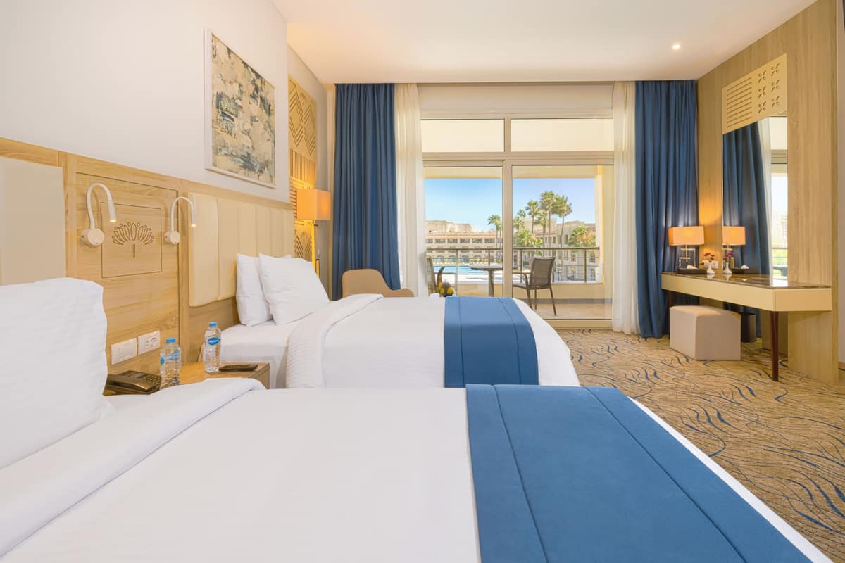 A hotel room with two beds, a desk, and a view of a pool and palm trees.