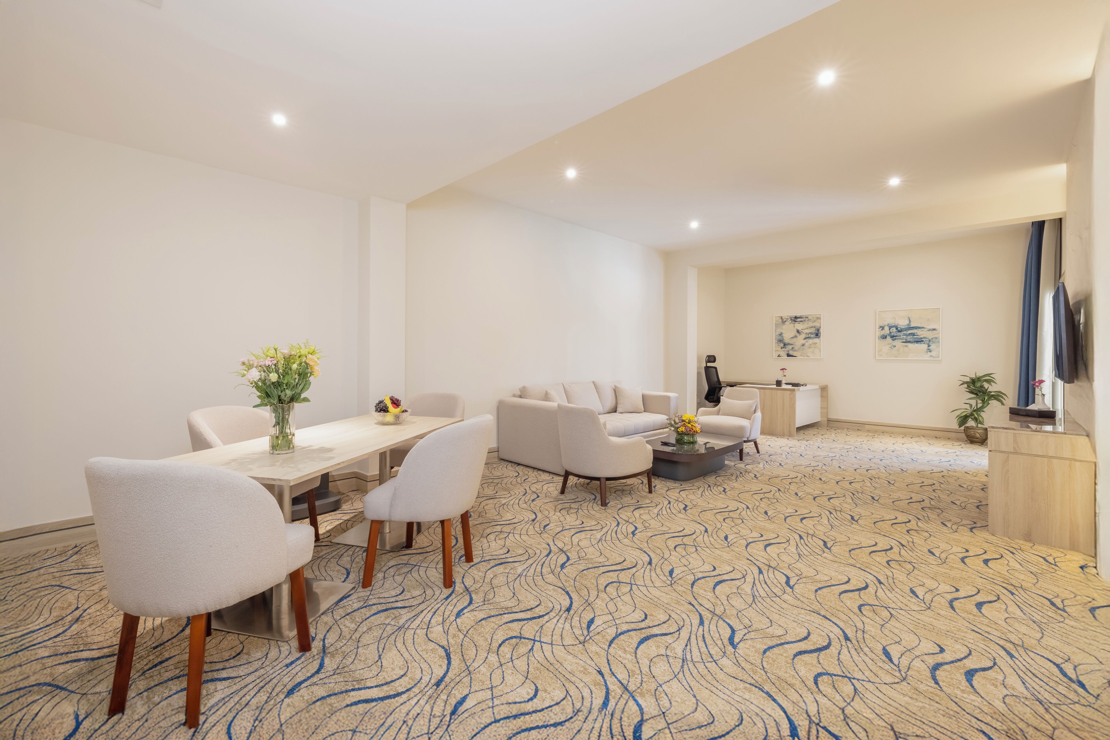 A hotel room with a dining area, a sofa set, a coffee table, and a desk with a chair.