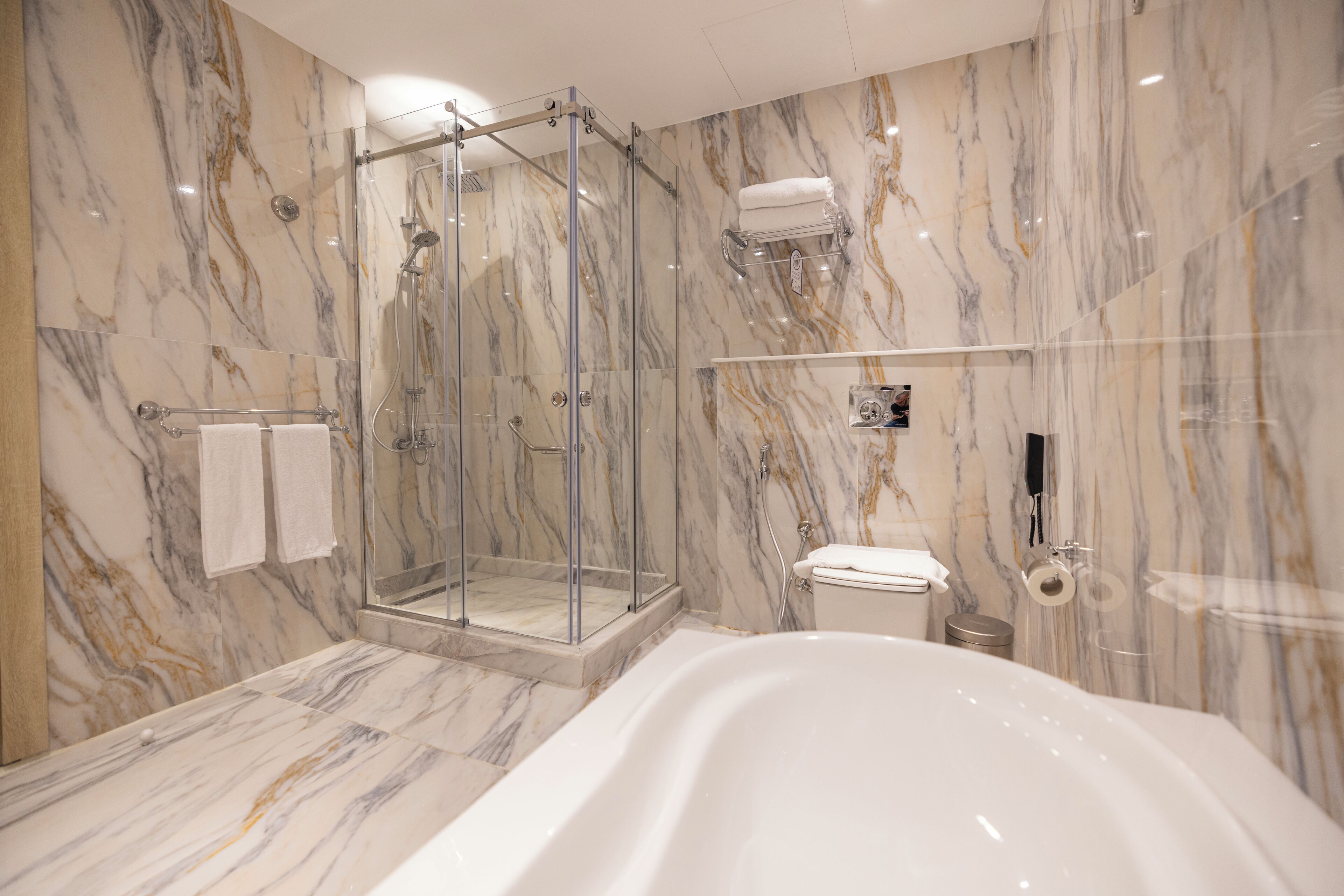 A modern bathroom with a glass-enclosed shower, a freestanding bathtub, and marble walls.