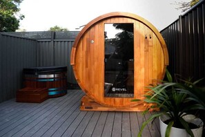 Un sauna en bois avec une porte en verre, un jacuzzi et une plante en pot, le tout installé dans un jardin.
