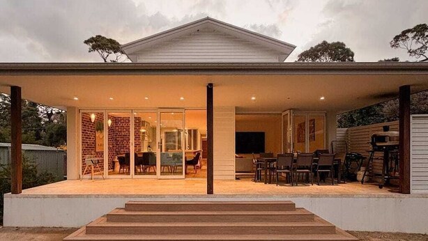 Une maison moderne dotée d’un patio couvert, d’un intérieur visible avec du mobilier et d’une pelouse bien entretenue.