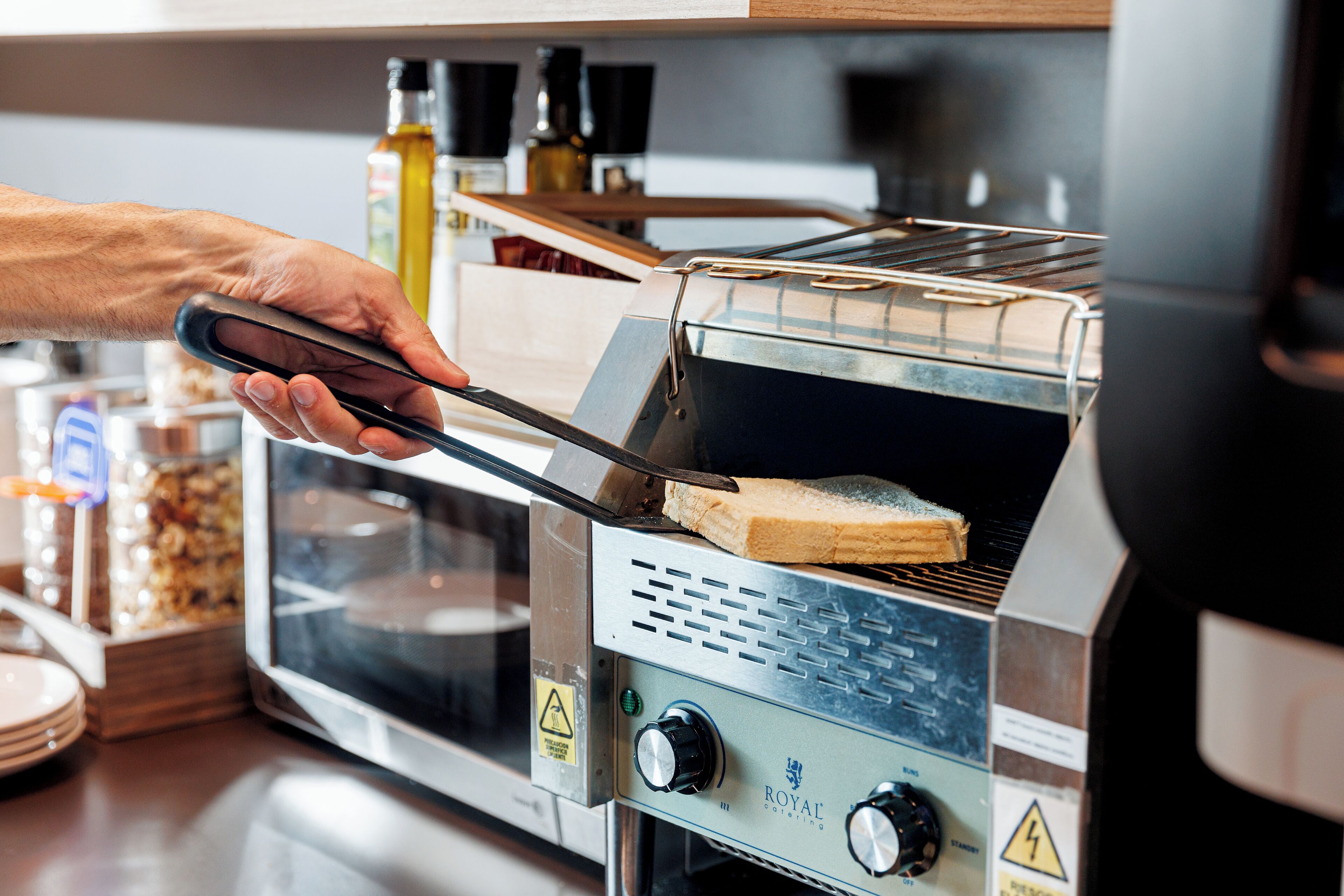 Una persona usando unas pinzas para colocar una rebanada de pan en un horno tostador.