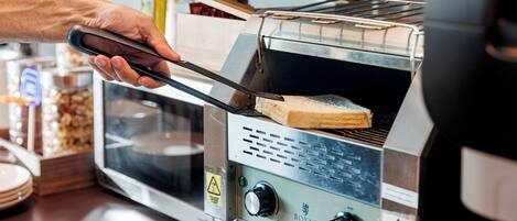 Una persona usando unas pinzas para colocar una rebanada de pan en un horno tostador.