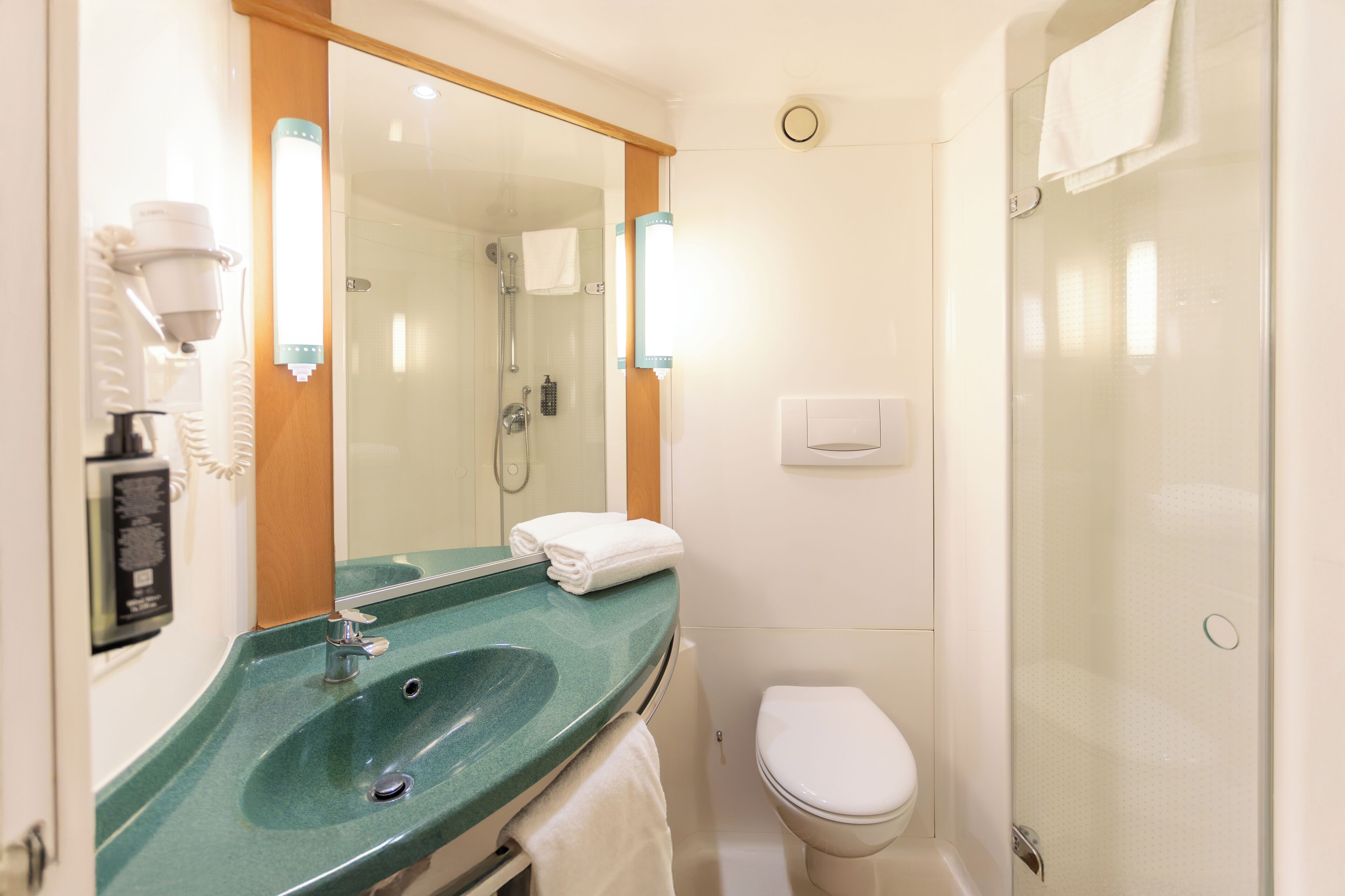 A bathroom with a green sink, a white toilet, and a glass shower enclosure.