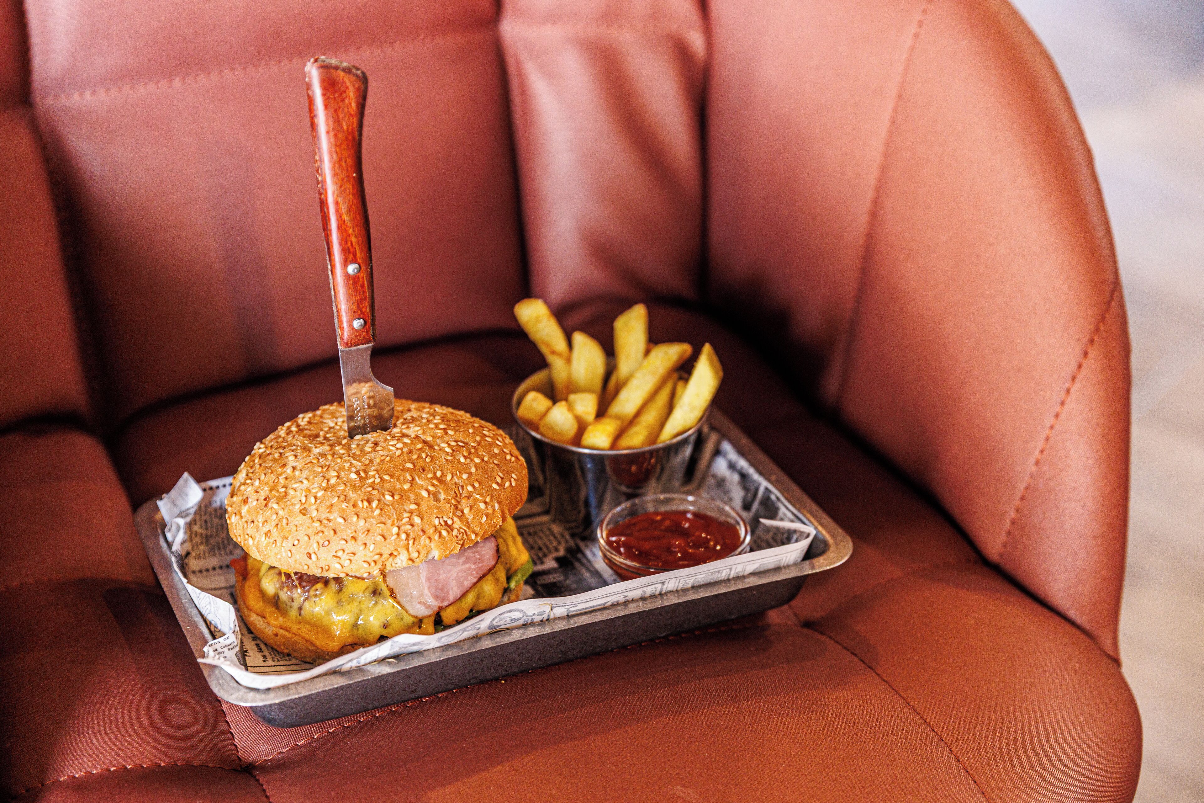 Una hamburguesa con papas fritas sobre una bandeja, colocada en un sillón de cuero.
