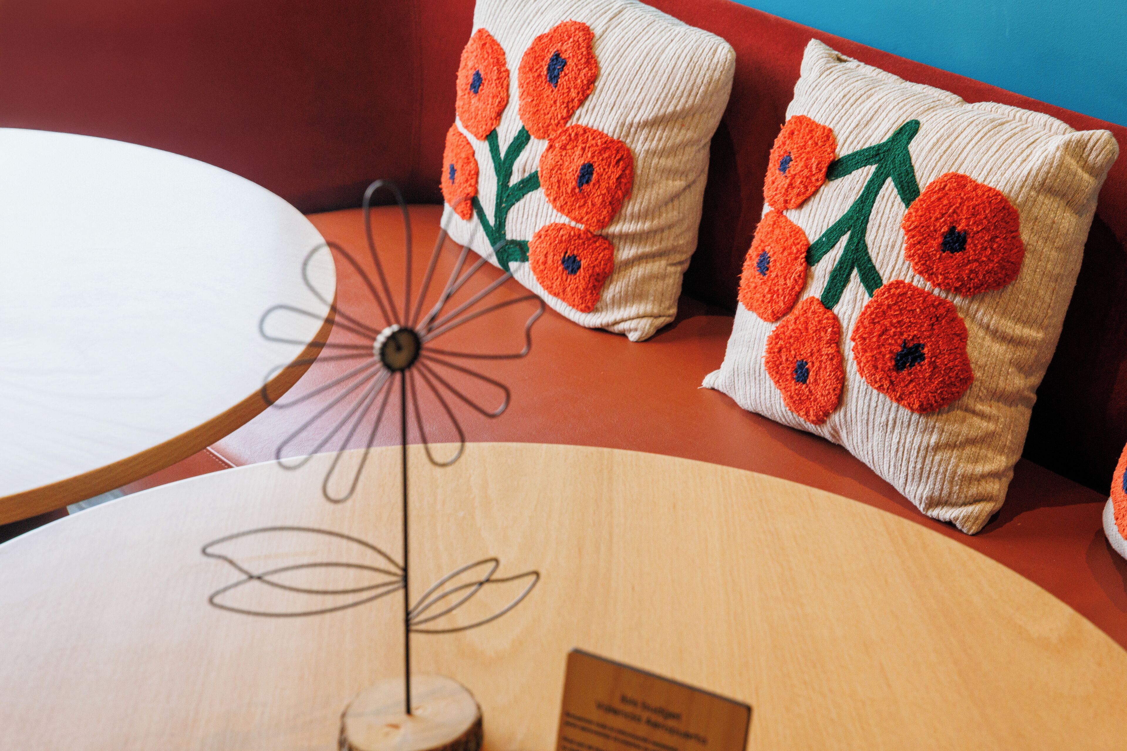 Una mesa redonda de madera con un centro de mesa decorativo de metal con forma de flor y dos cojines con flores naranjas.