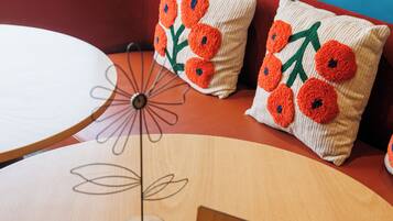 Una mesa redonda de madera con un centro de mesa decorativo de metal con forma de flor y dos cojines con flores naranjas.