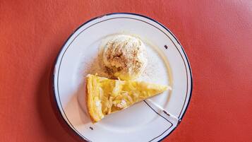 Un plato con una porción de pastel y una bola de helado sobre un plato blanco con borde azul, sobre un fondo rojo.