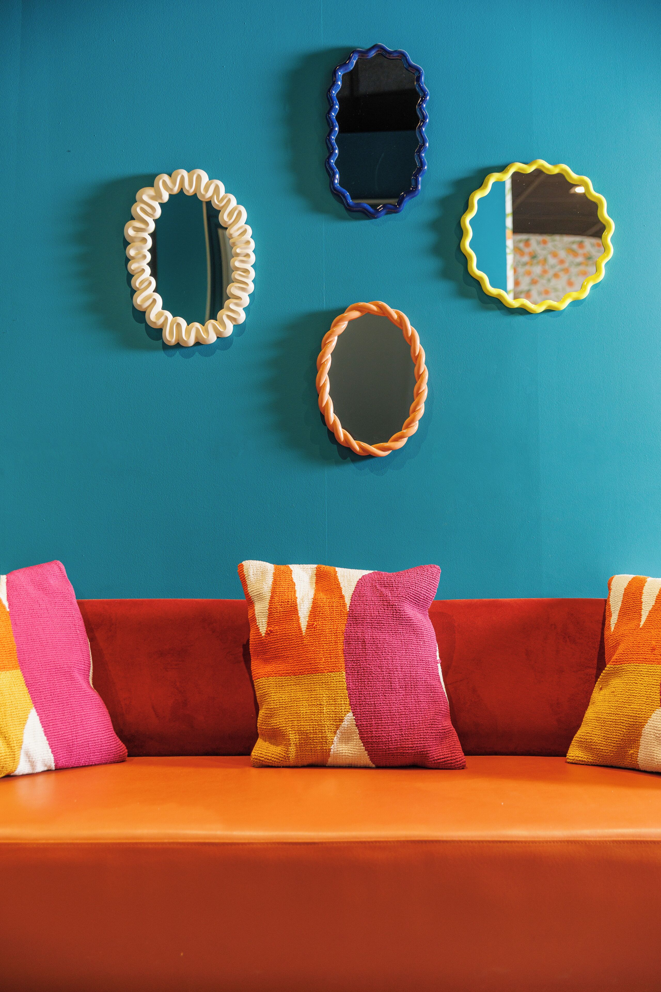 Una habitación con una pared verde azulado, un sofá rojo y cuatro espejos con distintos diseños de marco.