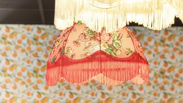 A table with a vase of yellow tulips, a hanging red fringe umbrella, and a patterned wallpaper background.