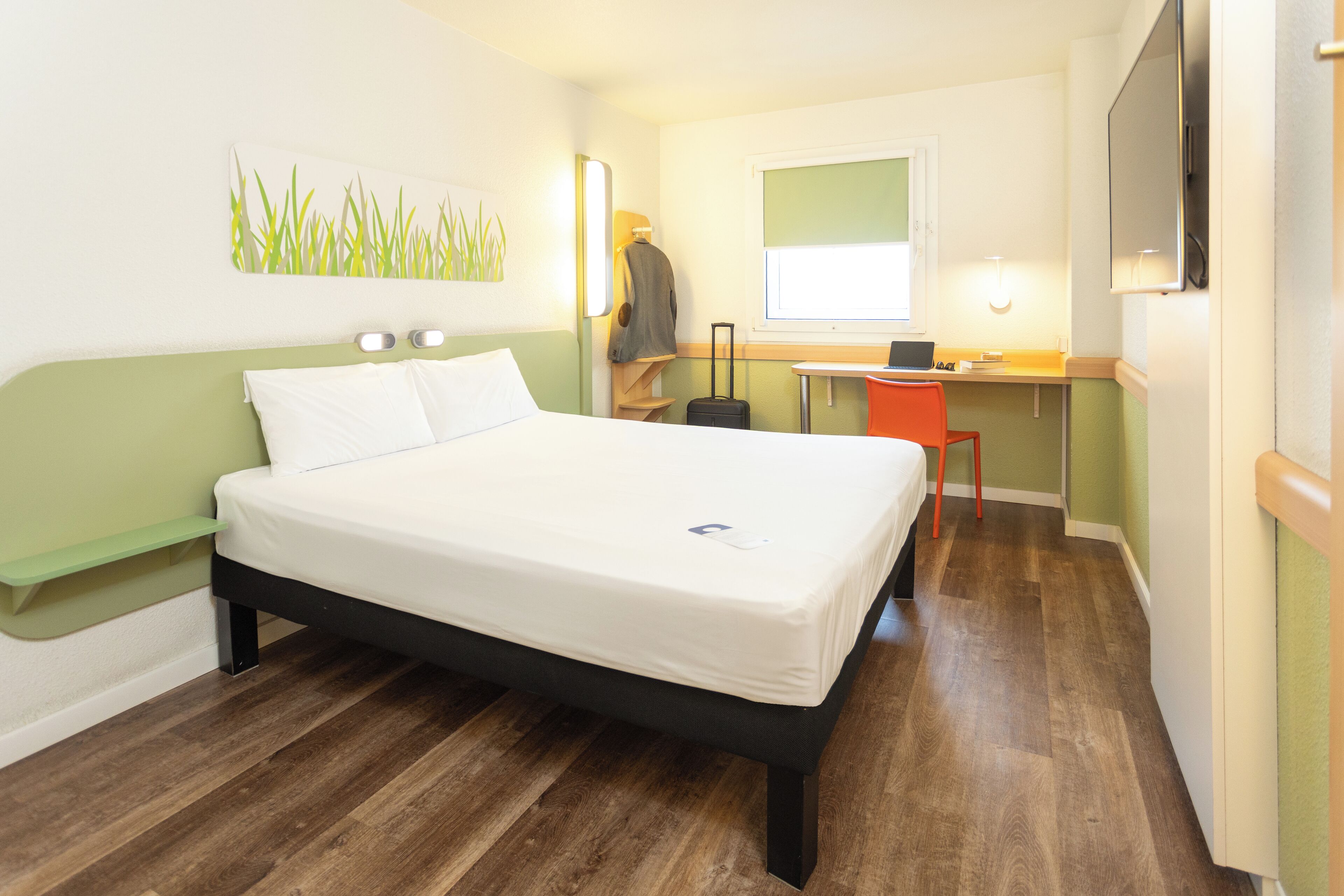 A hotel room with a bed, desk, chair, and a small table.