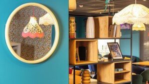 A room with a teal wall, a round mirror with a floral lampshade, and a wooden bookshelf with various items. - Ibis Budget Valencia Aeropuerto (Manises)