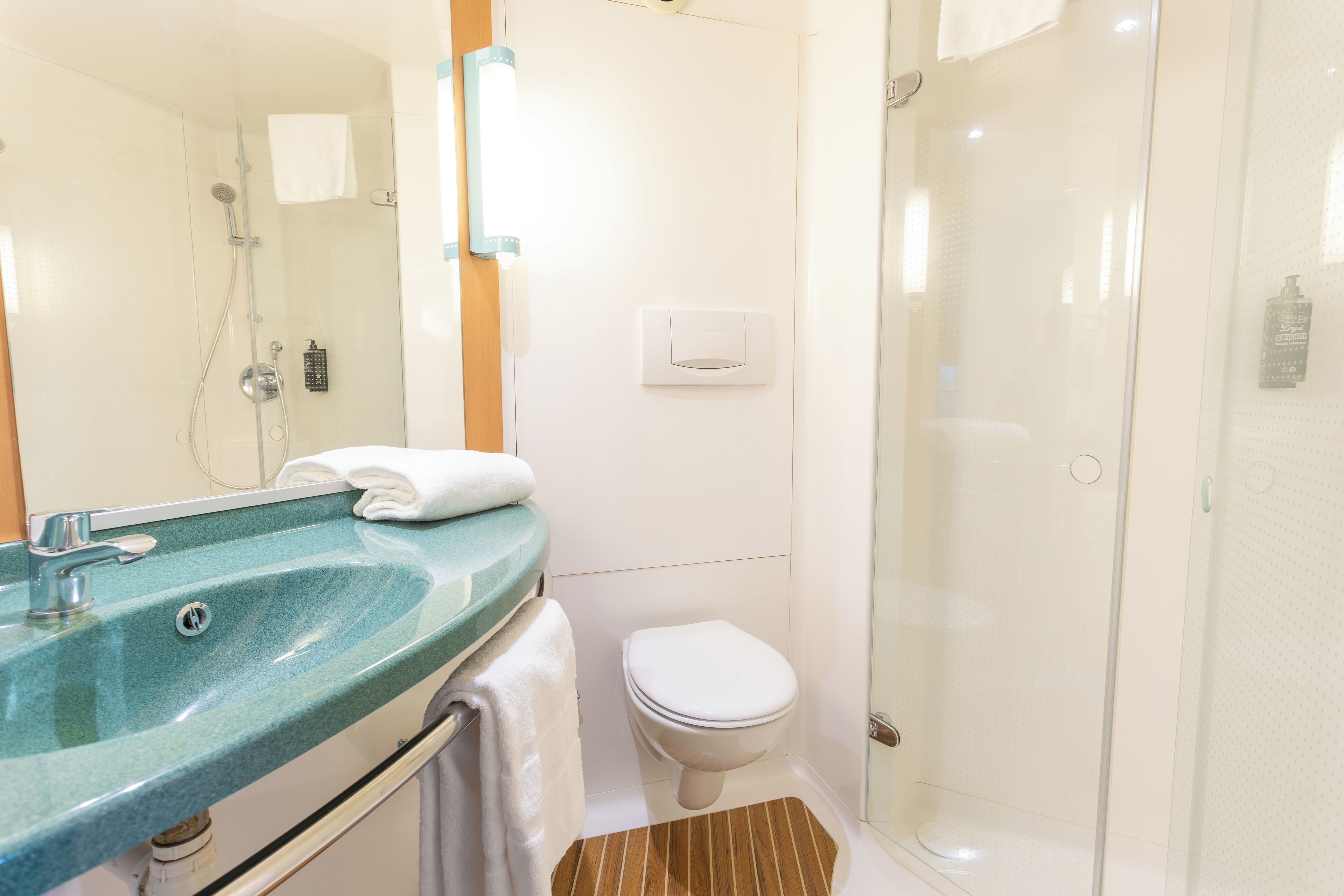 Un baño con cabina de ducha de vidrio, un lavamanos con encimera verde y un inodoro blanco.