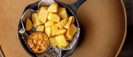 A cast iron skillet filled with golden potato wedges and a bowl of dipping sauce, placed on a brown surface.