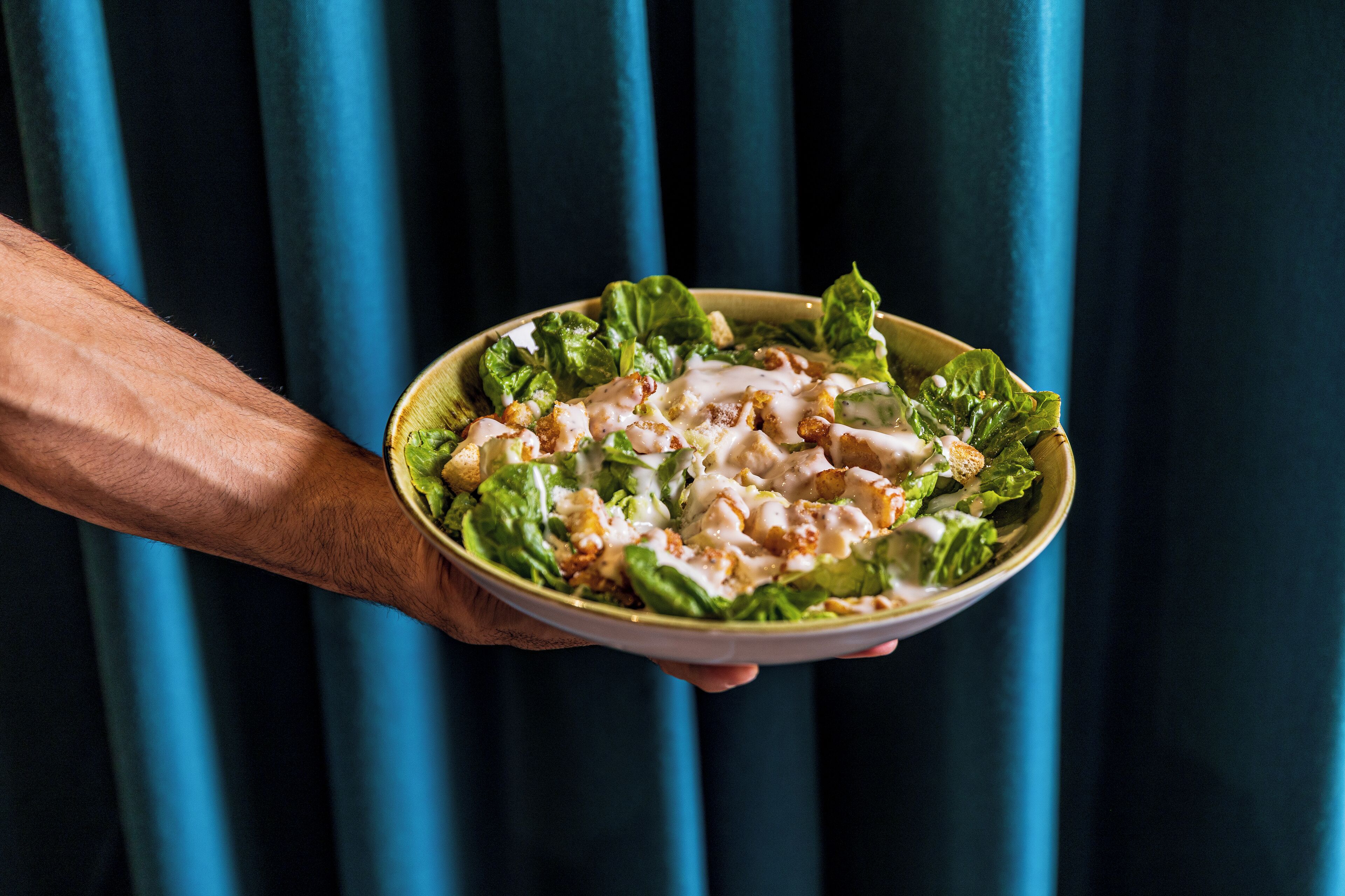 A person holding a bowl of salad with lettuce and a creamy dressing.
