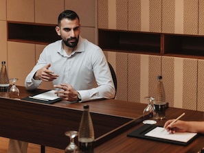 Een man zit aan een houten tafel met een notitieboek, pen en glazen flessen.