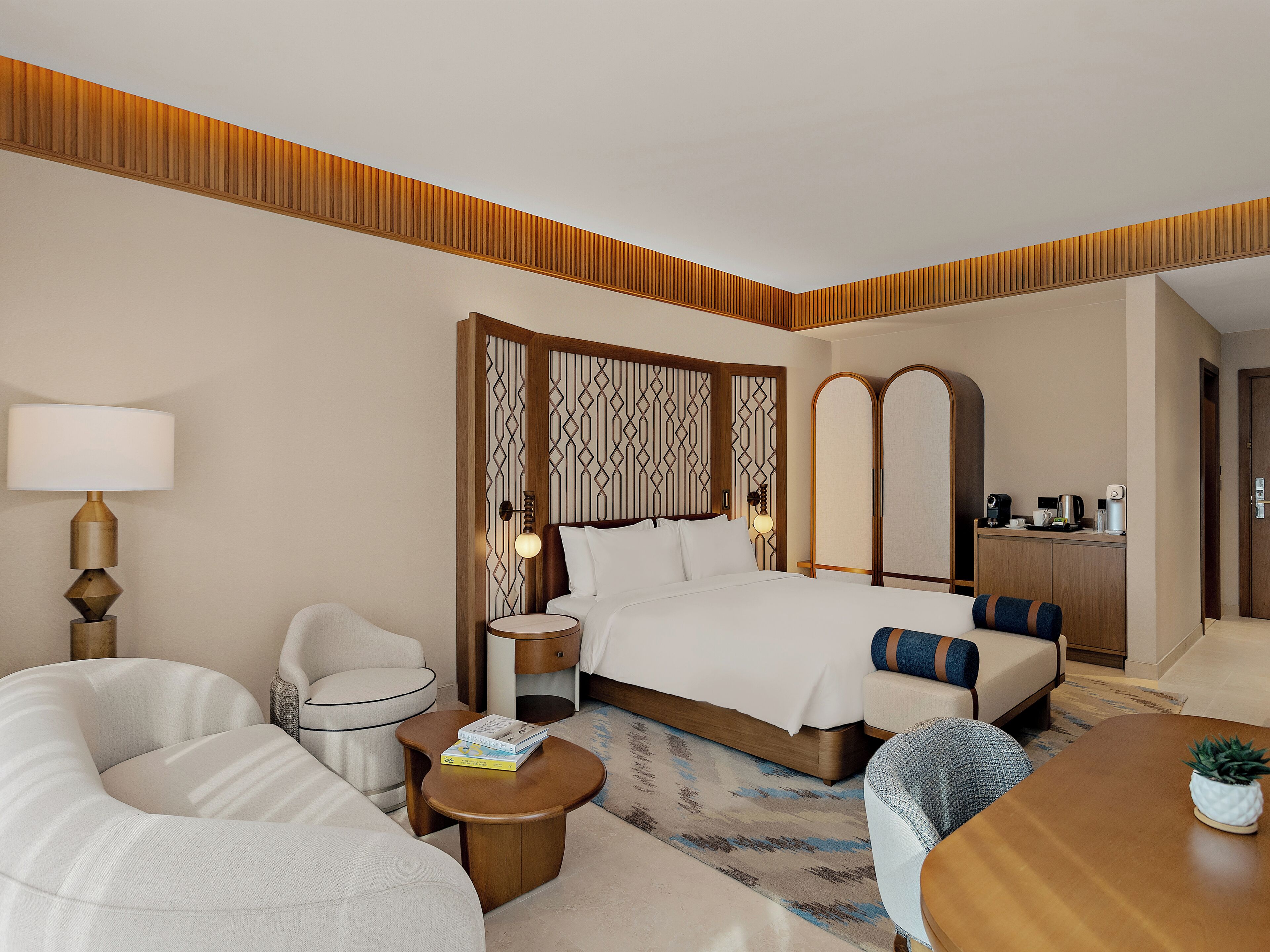 Une chambre d’hôtel comprenant un lit, un canapé, une petite table, une lampe, un miroir et un coin cuisine.