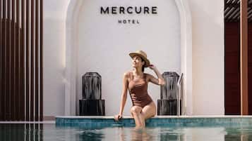 Una mujer en traje de baño sentada junto a una piscina, con un cartel que dice 'Mercure Hotel' al fondo.