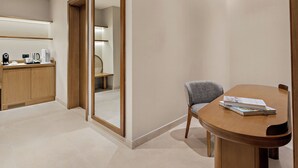 Una habitación de hotel moderna con una mesa de comedor de madera, una silla, una pequeña cocina con una cafetera y un espejo grande.