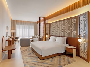 Quarto de hotel moderno com uma cama grande, uma escrivaninha, uma cadeira e um sofá.