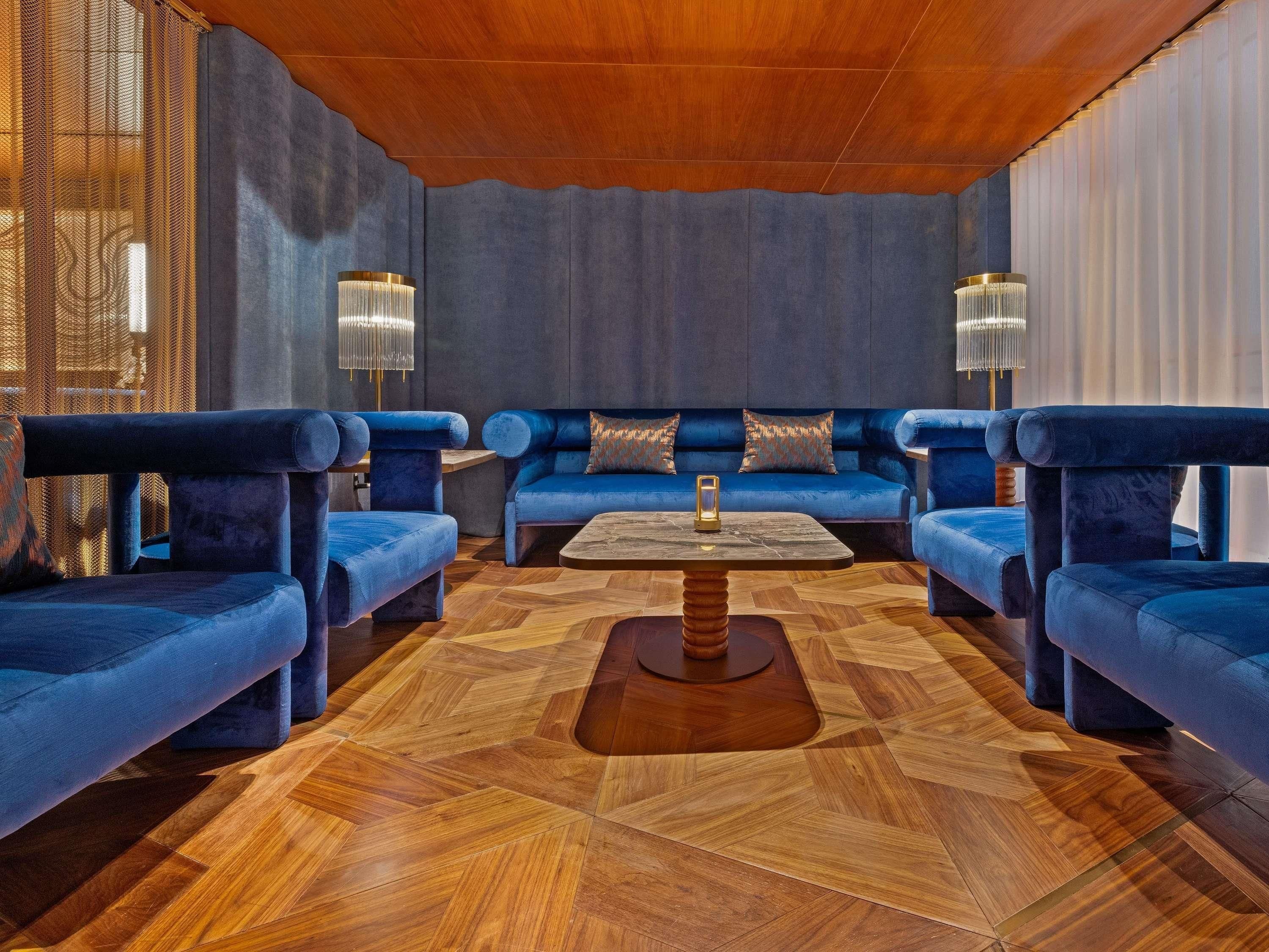 A modern lounge area with a geometric patterned floor, blue upholstered seating, and two floor lamps.
