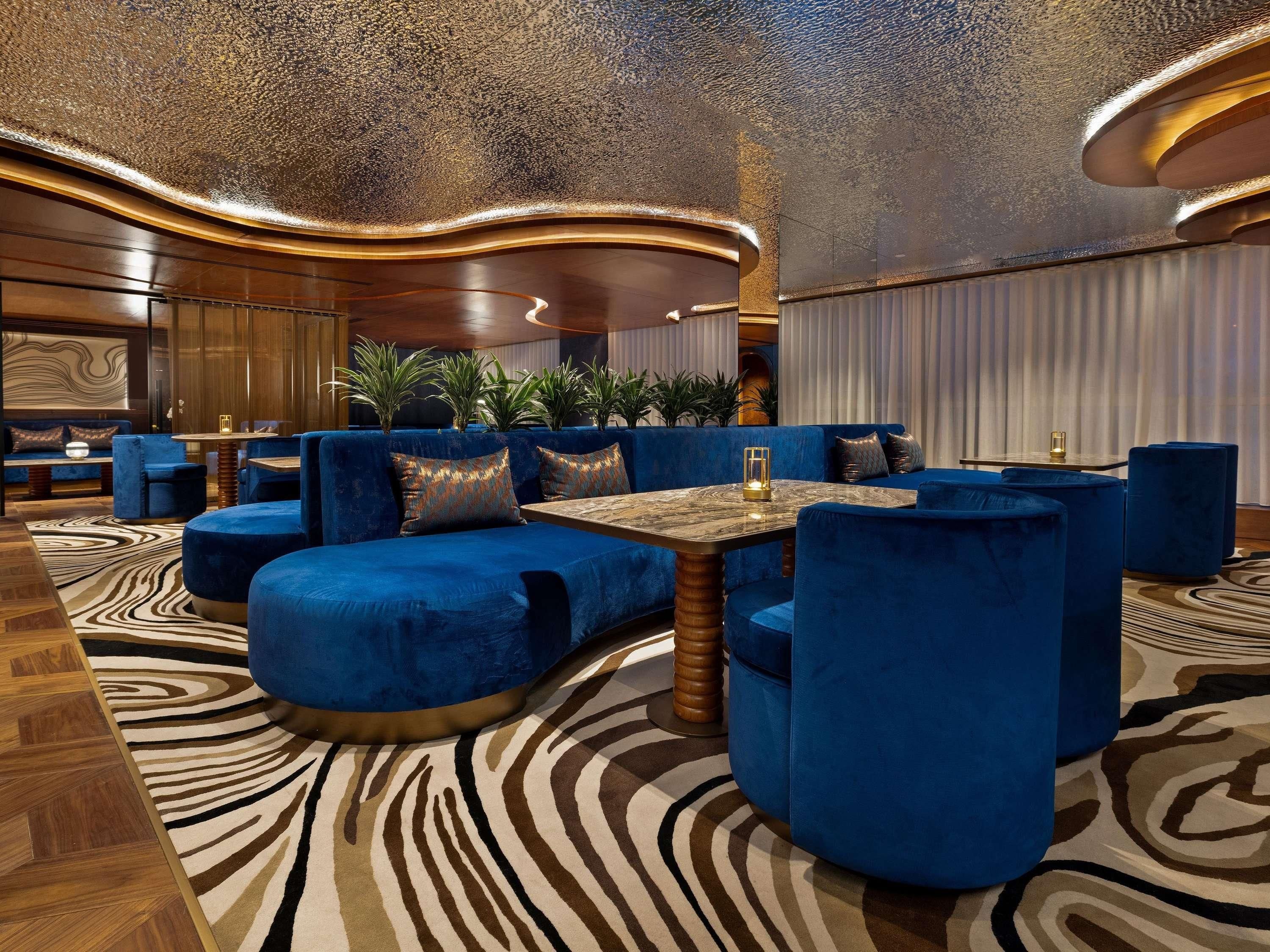 A modern lounge area with blue upholstered seating, a patterned carpet, and a decorative ceiling.