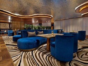 Un espace détente moderne avec des sièges bleus rembourrés, une moquette à motifs et un plafond décoratif.
