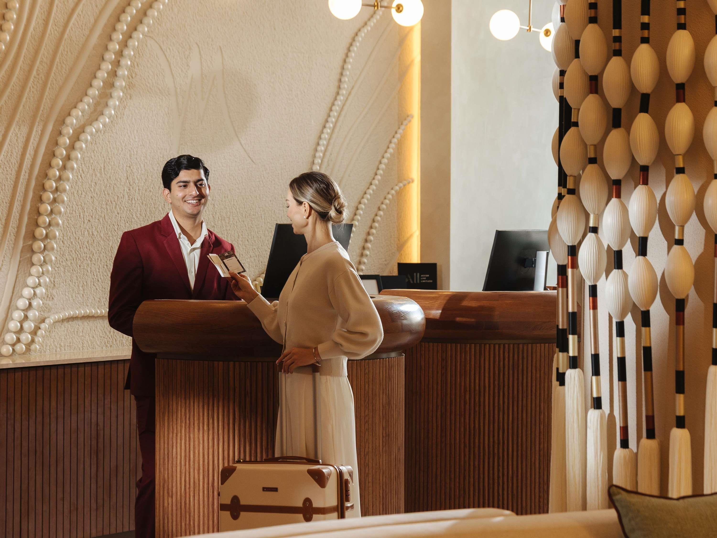 Un mostrador de recepción con detalles de madera, una zona de registro y una pared decorada con una guirnalda de perlas.