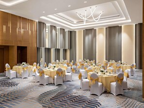 Une salle de banquet avec des tables rondes, des chaises blanches ornées de rubans dorés et un tapis à motifs.