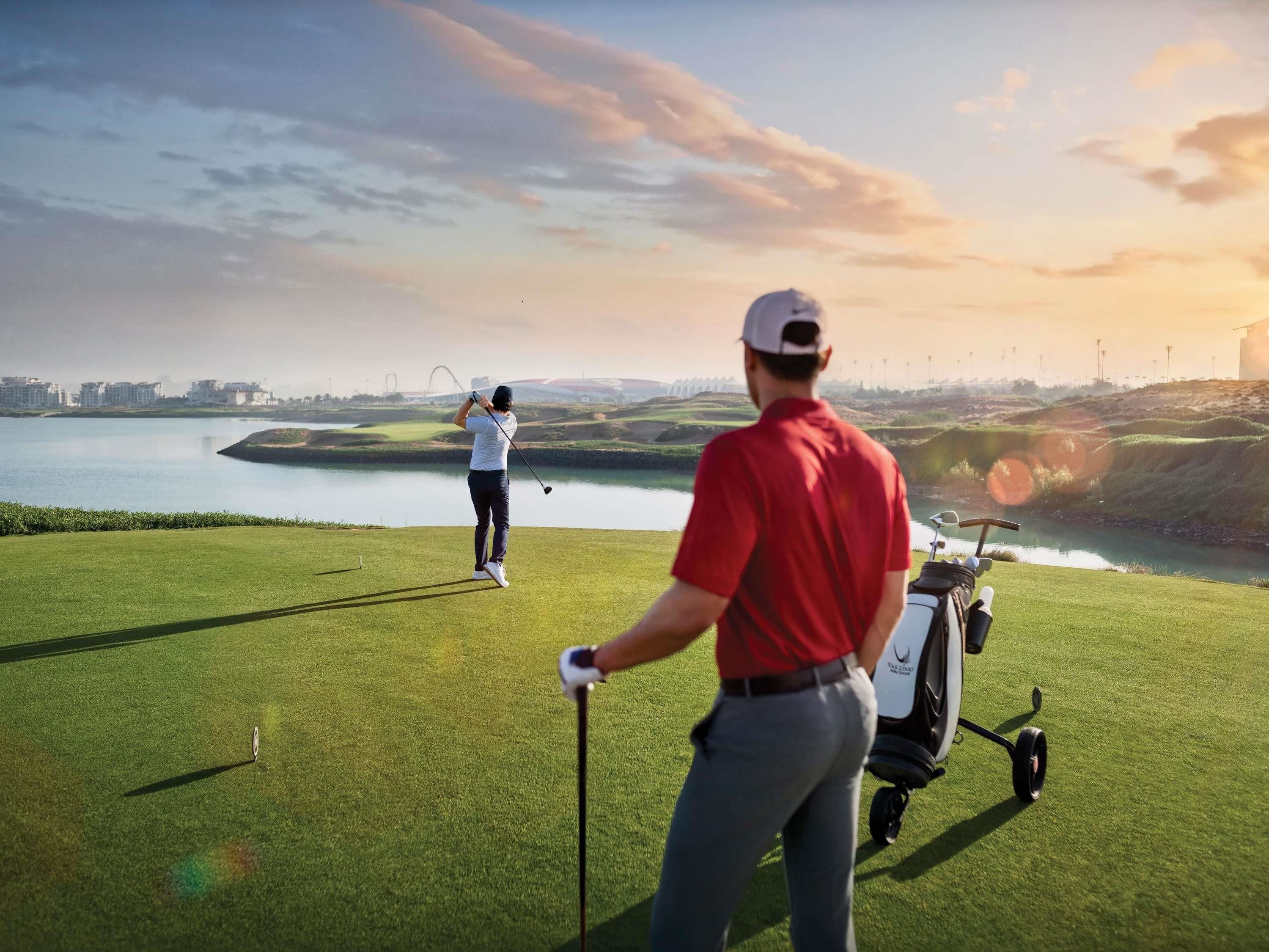 Un terrain de golf avec un plan d’eau en arrière-plan, un chariot de golf et un golfeur portant un maillot rouge.