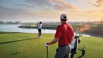 A golf course with a water body in the background, a golf cart, and a golfer in a red shirt.