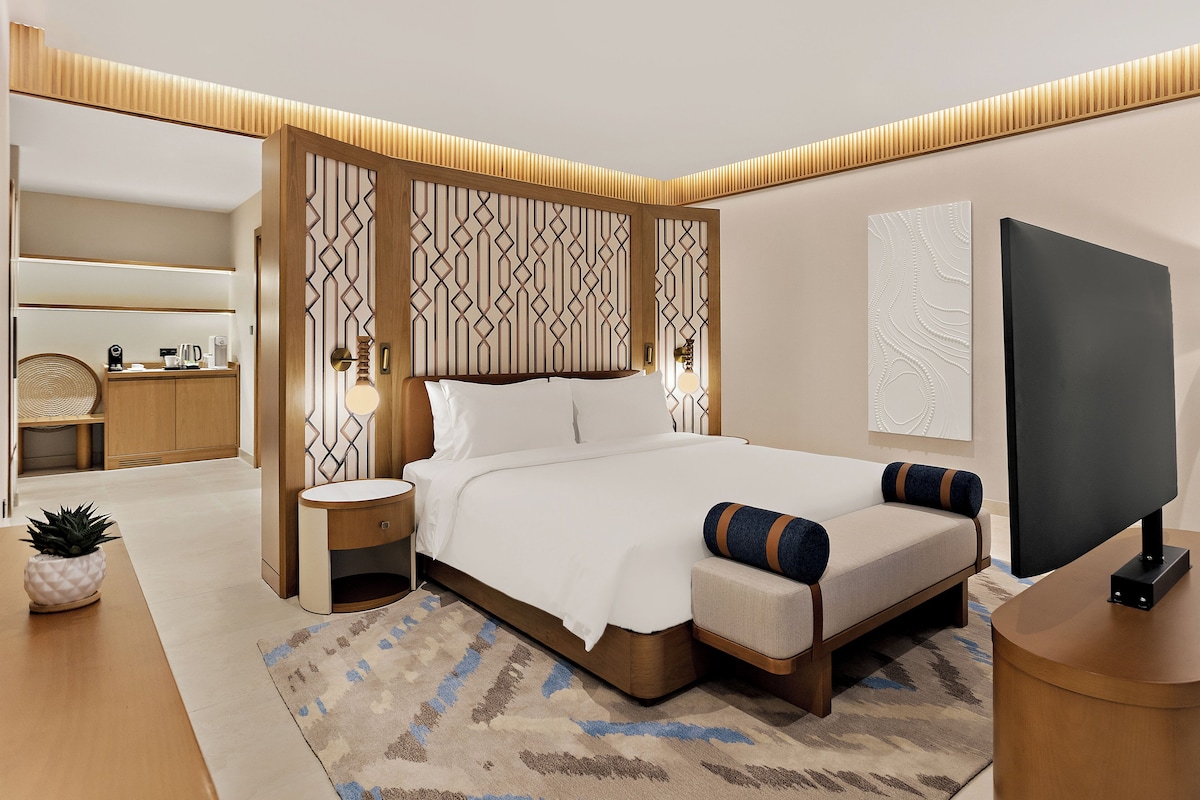 Una habitación de hotel moderna con una cama grande, mesitas de noche, un televisor y un panel decorativo en la pared.