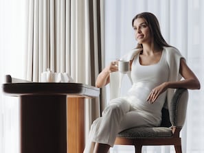 A person seated by a table with a coffee maker, a cup, and a book.