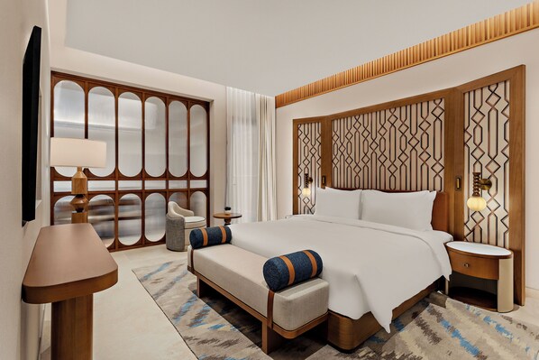 Una habitación de hotel moderna con una cama grande, mesitas de noche, un sofá, una lámpara y un separador decorativo.