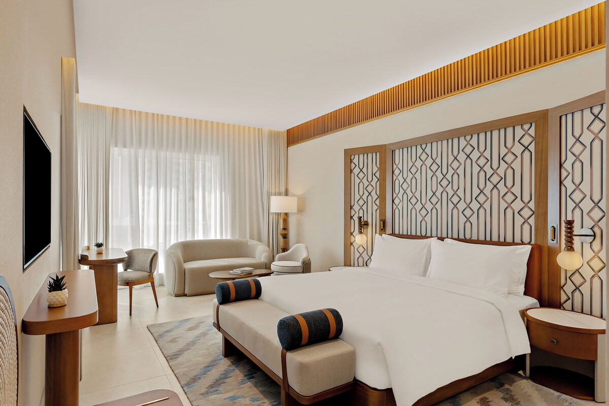 Una habitación de hotel con una cama grande, dos sillones, una mesita y un televisor.