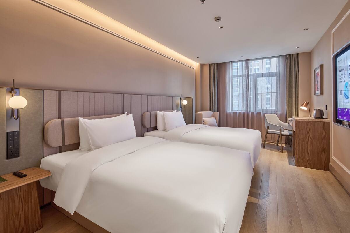 A hotel room with two beds, a desk, a chair, a TV, and a window with curtains.